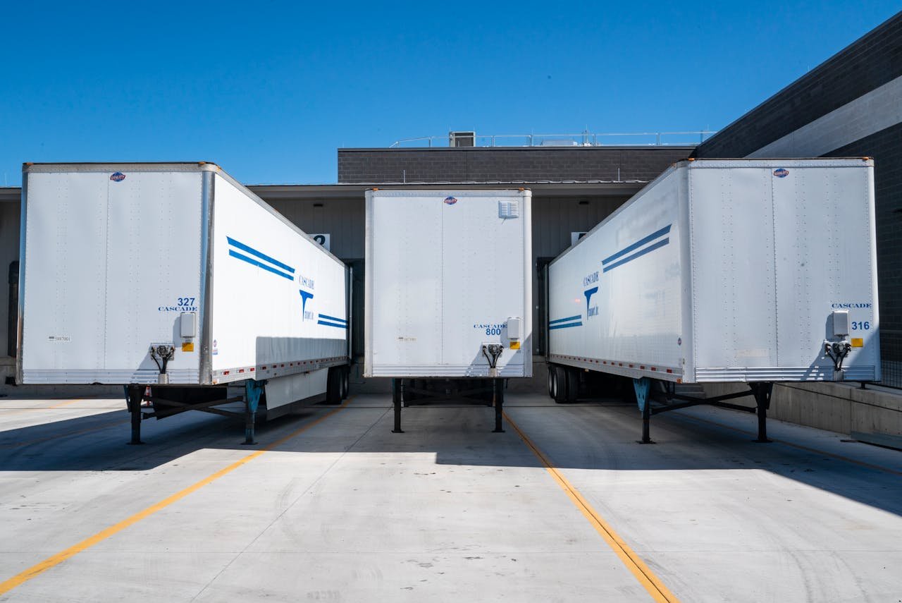 Inicio Three white cargo trailers parked at an industrial shipping dock under clear blue skies.