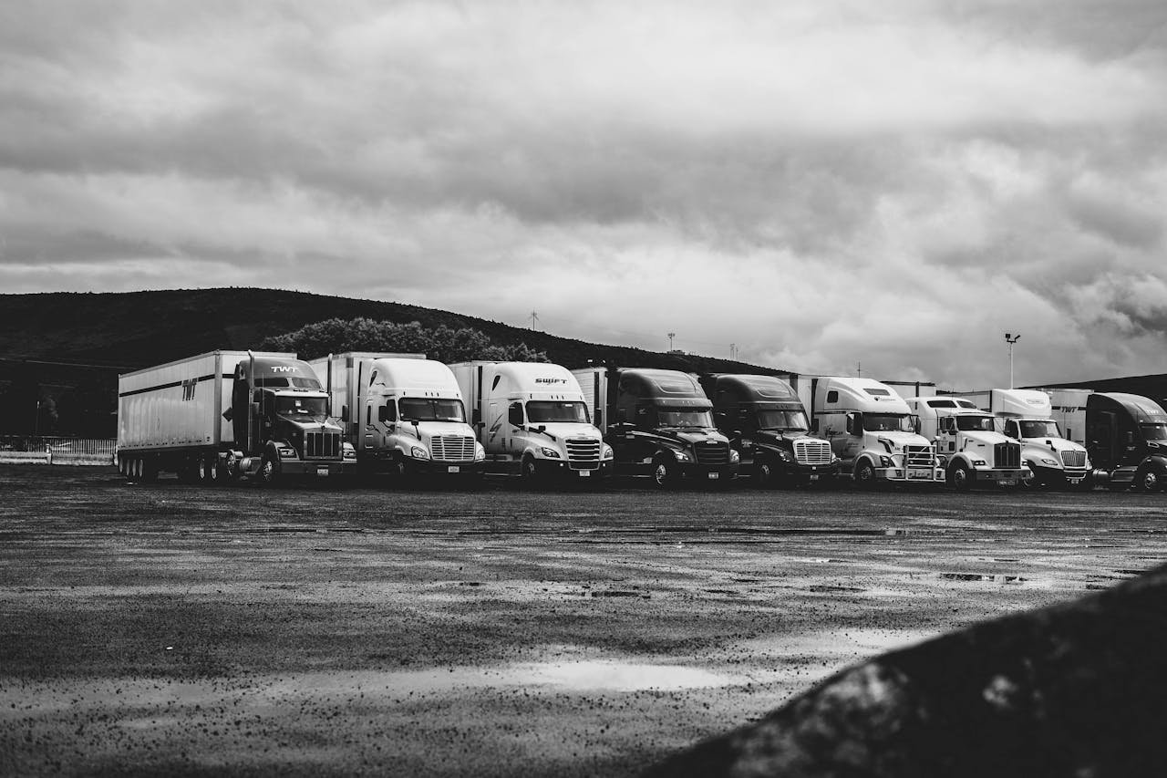 Inicio Row of parked semi trucks in a rainy lot, captured in a dramatic black and white setting.