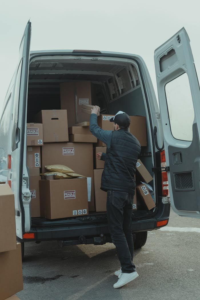 Inicio A courier organizing boxes in a delivery van for shipment on a cloudy day.