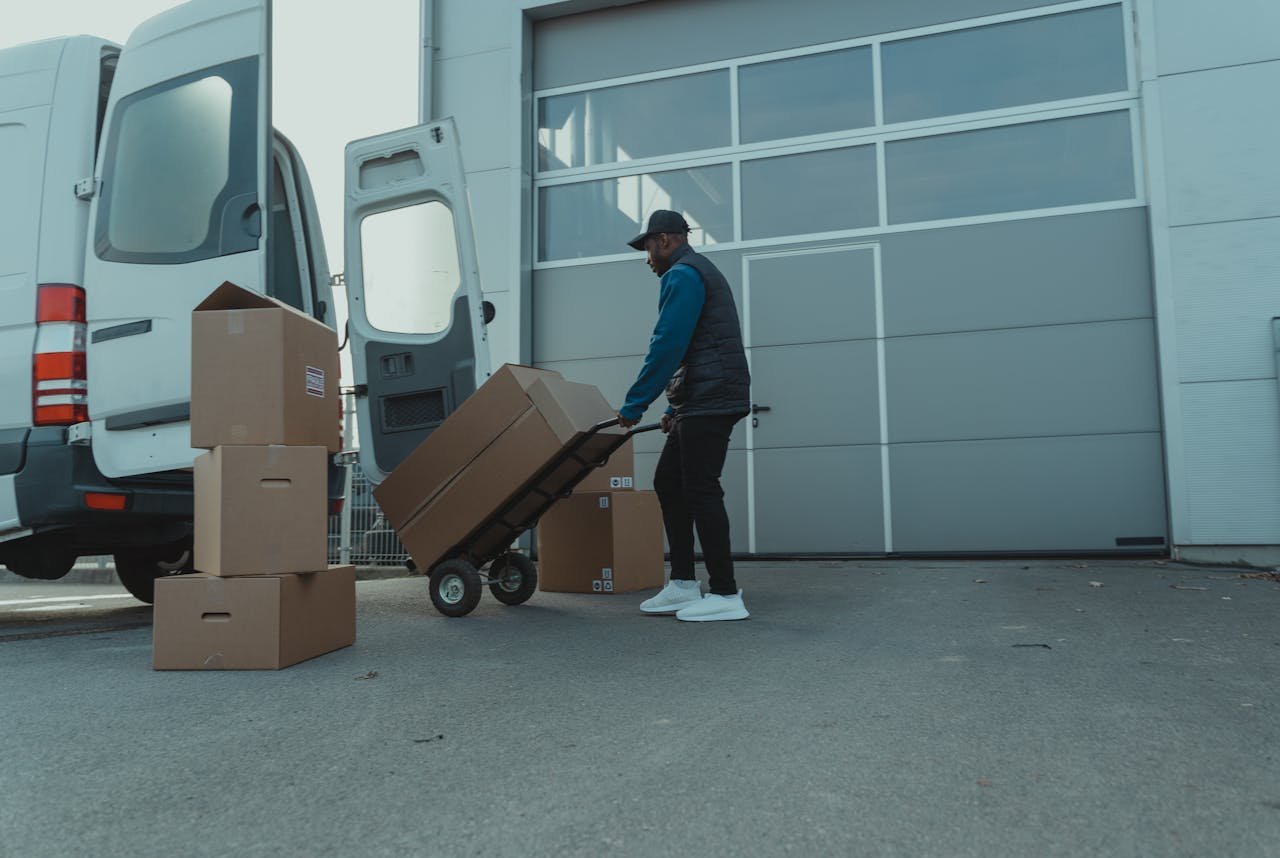 Acerca de Courier unloading packages from a delivery van at a warehouse entrance. Efficient distribution.